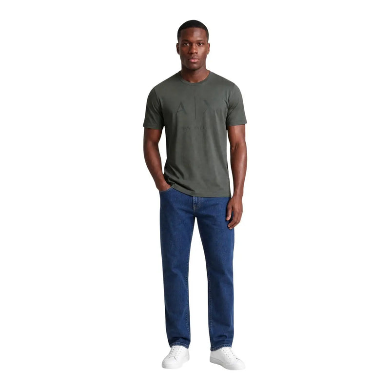 Ein Mann, der einen Armani Exchange Grünes Herren-T-Shirt aus Baumwolle mit schwarzem Grafikdetail, kombiniert mit blauen Jeans und weißen Sneakers