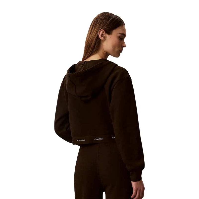 Rückseite eines dunkelbraunen, kurzen Baumwoll-Hoodies mit einem dezenten weißen Calvin Klein-Logo im unteren Rückenbereich.