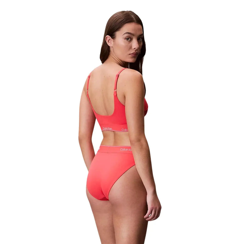 Korallenrosa Calvin Klein Bikini-Set mit dünnen Trägern und Markenlogo am Bund, dazu ein orangefarbenes Calvin Klein Jeans-Damen-Bralette und Strandmode.