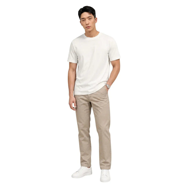 Ein Mann, der beige Baumwollhosen von Calvin Klein und ein schlichtes weißes Kurzarmhemd trägt t-shirt