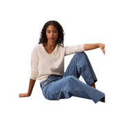 Frau in blauer Calvin Klein Damen-Jeans aus Baumwoll-Denim mit weitem Bein und einem cremefarbenen V-Ausschnitt-Pullover, Vorderansicht