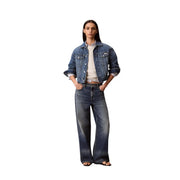 Eine Frau, die eine dunkelblaue Jeansjacke mit hochgekrempelten Ärmeln und eine weite Jeans mit einem weißen Baumwoll-Sweatshirt von Calvin Klein trägt.