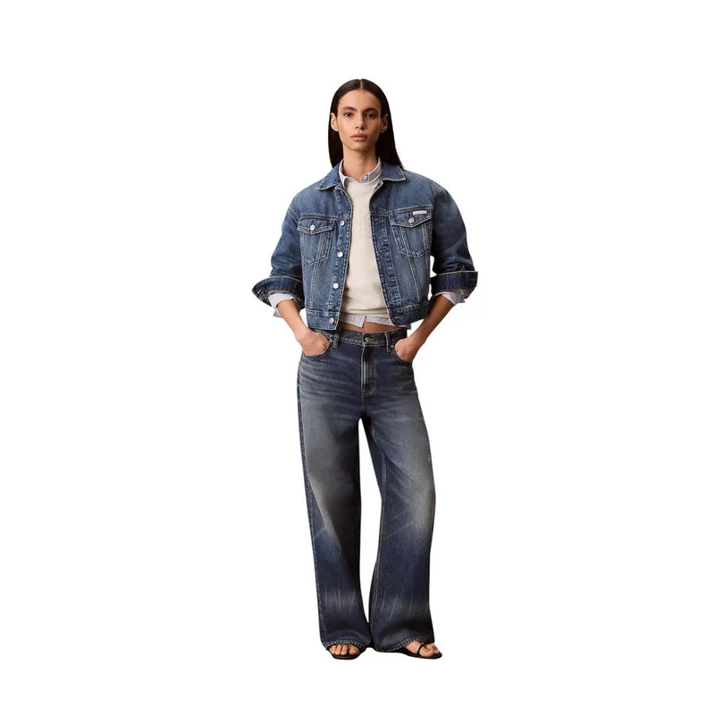 Eine Frau, die eine dunkelblaue Jeansjacke mit hochgekrempelten Ärmeln und eine weite Jeans mit einem weißen Baumwoll-Sweatshirt von Calvin Klein trägt.