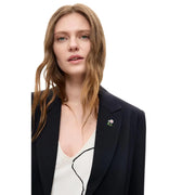 Eine zarte, florale Metallbrosche mit weißer Blüte und grünem Stiel an einem schwarzen Desigual-Damenblazer aus Viskosemischung mit langem Revers