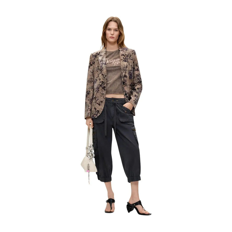 Eine Frau trägt einen beigefarbenen Polyesterblazer von Desigual mit braunem Blumenmuster über einem passenden kurzen T-Shirt.