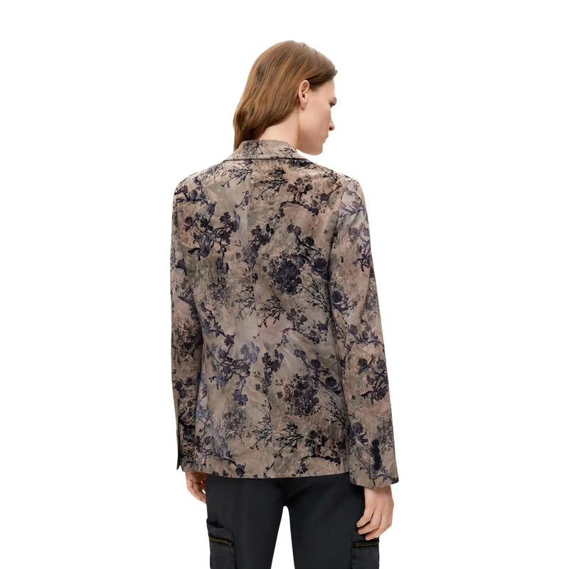Eine Frau trägt einen beigefarbenen Polyesterblazer von Desigual mit langen Ärmeln und einem eleganten, dezenten Blumenmuster.