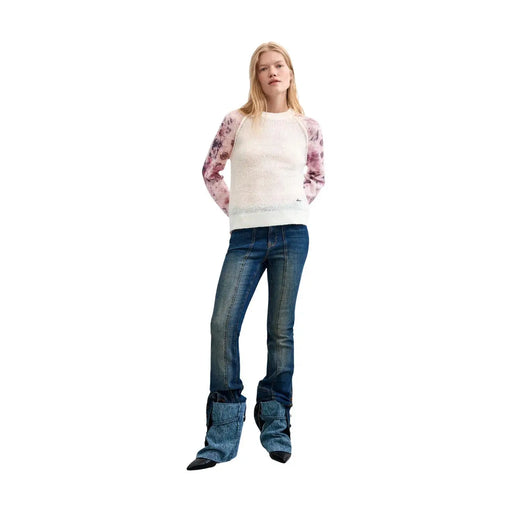 Eine Frau trägt einen weißen Desigual-Damenpullover aus Wollmischung mit Blumenmuster und rosa geblümten Ärmeln sowie eine dunkelblaue Schlagjeans.