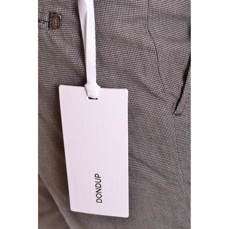 Ein weißes, rechteckiges Markenetikett mit schwarzem Aufdruck „dondup“ ist mit einem weißen Band an einer grauen Herren-Baumwollhose mit Hahnentrittmuster befestigt.