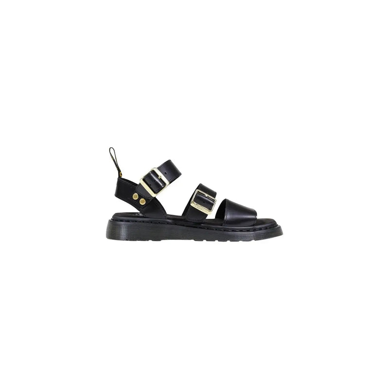 Schwarze Dr. Martens Damen-Sandalen aus Leder mit goldfarbenen Schnallen und einer von hinten sichtbaren, klobigen Gummisohle.