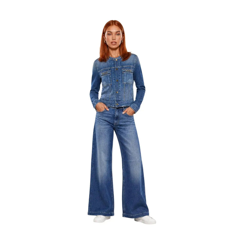 Eine Frau trägt eine Guess Damen-Blazer aus blauer Baumwolle, Modell Ivy, mit zwei Brusttaschen und passender Jeans in mittlerer Waschung.