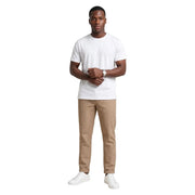 Ein Mann trägt ein weißes Baumwoll-T-Shirt von Hydra Men mit Rundhalsausschnitt, beige Nadelstreifenhosen und weiße Turnschuhe.