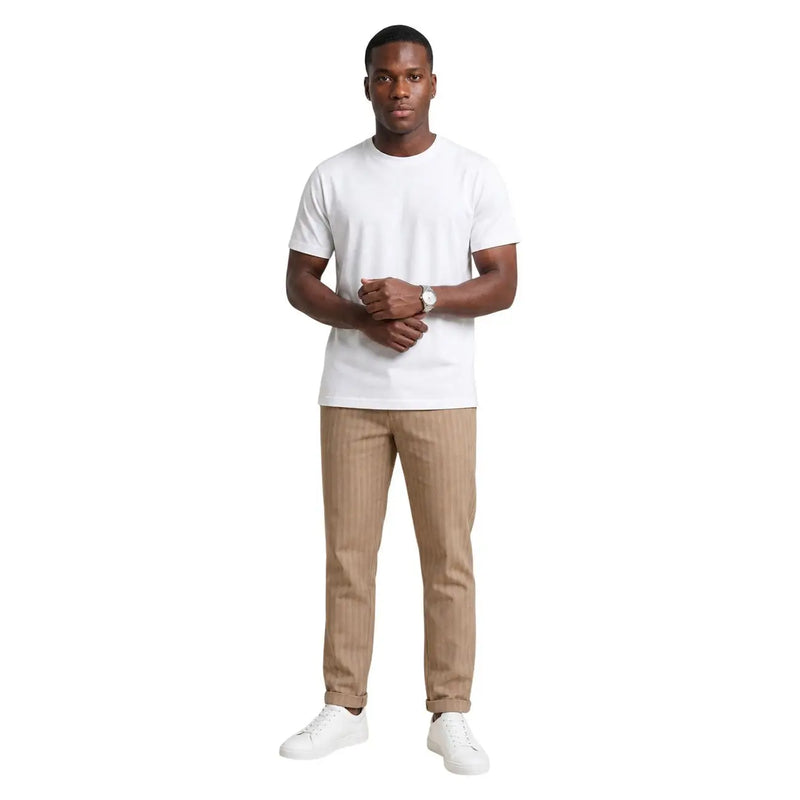 Ein Mann trägt ein weißes Baumwoll-T-Shirt von Hydra Men mit Rundhalsausschnitt, beige Nadelstreifenhosen und weiße Turnschuhe.