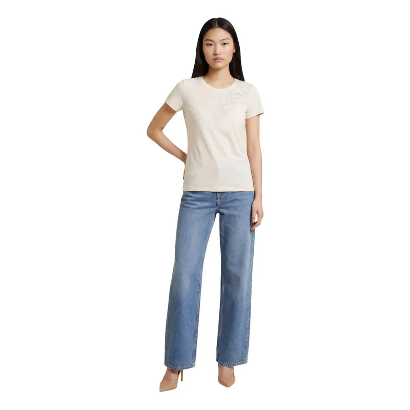 Eine Frau trägt ein beigefarbenes, kurzes Baumwoll-T-Shirt von Liu Jo mit Rundhalsausschnitt und gesticktem Logo sowie hellblaue Jeans.