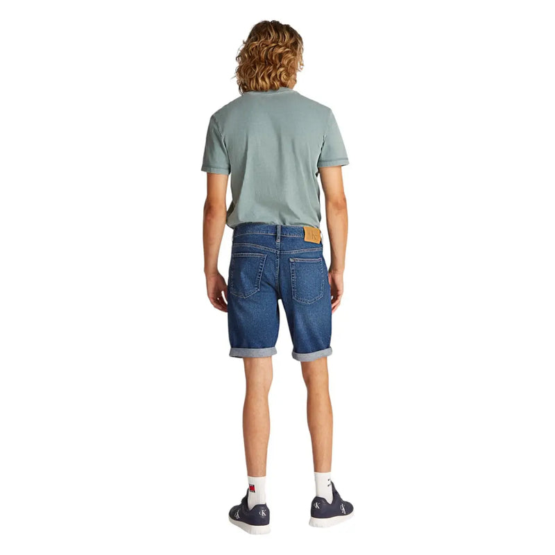 Mens blue denim shorts shown from the back with rolled cuffs and a tan leather brand patch on the waistband