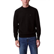 Male model wearing a black crewneck sweater with gray long sleeve shirt and black pants