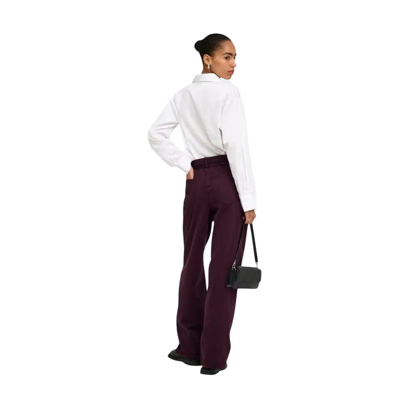 Eine elegante, schwarze Mini-Umhängetasche aus Leder mit minimalistischem Design und schmalem Riemen, die perfekt zu einer lilafarbenen Baumwolljeans mit Gürtel passt.
