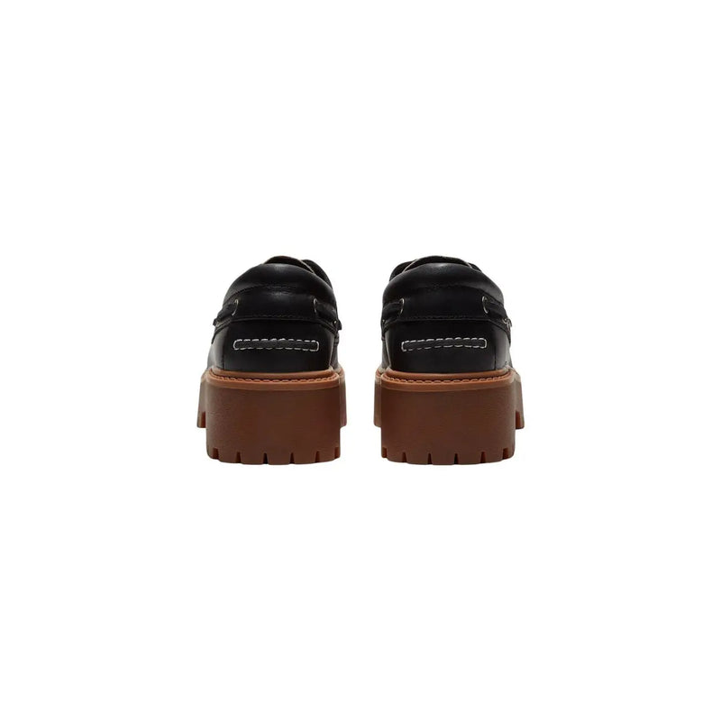 Timberland Schwarze Damen-Plateauschuhe aus Leder, bestehend aus schwarzen Lederloafers mit klobigen braunen Gummisohlen und weißen Ziernähten.