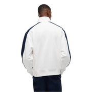 Weiße Lacoste-Trainingsjacke mit marineblauen Kontrasteinsätzen an Ärmeln und Schultern, kombiniert mit einer weiß gestreiften Tommy Hilfiger Jeans und einem Sweatshirt aus Bio-Baumwolle.