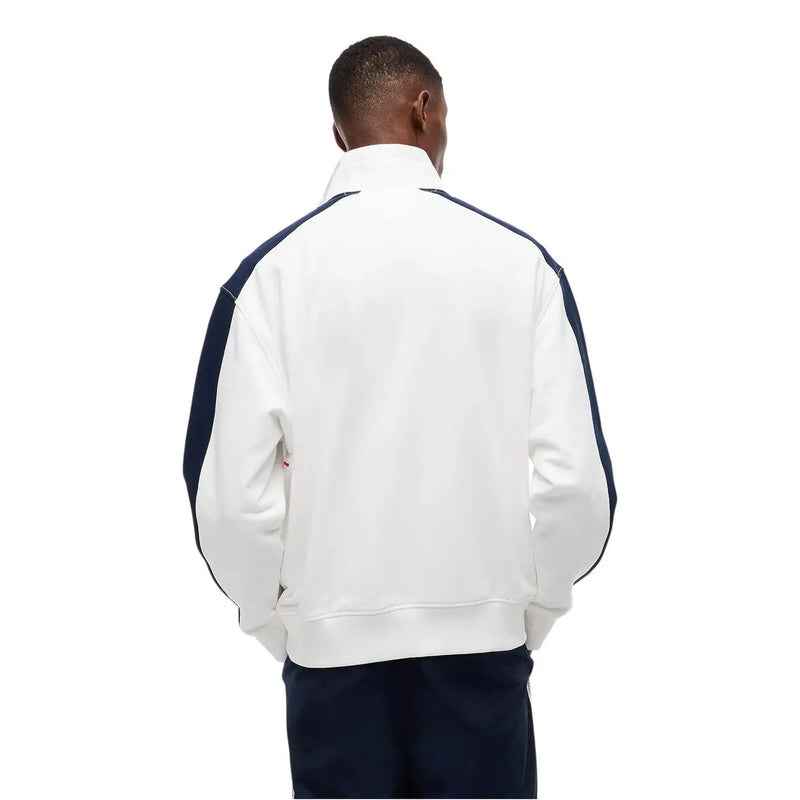 Weiße Lacoste-Trainingsjacke mit marineblauen Kontrasteinsätzen an Ärmeln und Schultern, kombiniert mit einer weiß gestreiften Tommy Hilfiger Jeans und einem Sweatshirt aus Bio-Baumwolle.