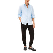 Hellblau-weiß gestreiftes Baumwollhemd mit hochgekrempelten Ärmeln und Knopfleiste, kombiniert mit einer schwarzen Baumwollhose von Tommy Hilfiger für Herren.