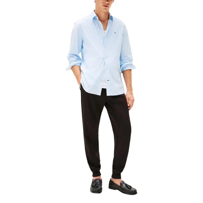 Hellblau-weiß gestreiftes Baumwollhemd mit hochgekrempelten Ärmeln und Knopfleiste, kombiniert mit einer schwarzen Baumwollhose von Tommy Hilfiger für Herren.