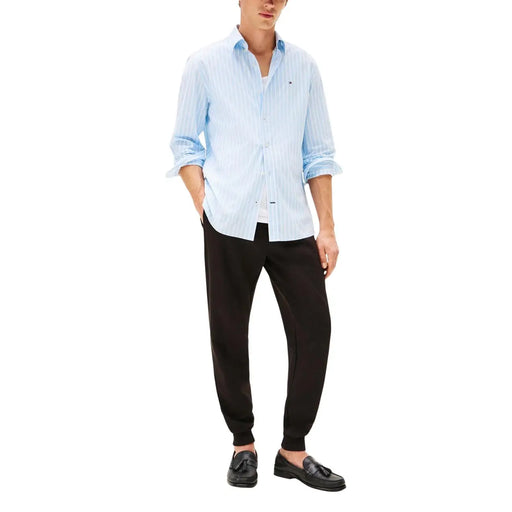 Hellblau-weiß gestreiftes Baumwollhemd mit hochgekrempelten Ärmeln und Knopfleiste, kombiniert mit einer schwarzen Baumwollhose von Tommy Hilfiger für Herren.