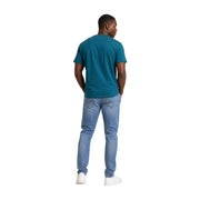 Ein Mann trägt ein türkisgrünes, kurzärmeliges T-Shirt aus Bio-Baumwolle, kombiniert mit hellen Jeans. Tommy Hilfiger