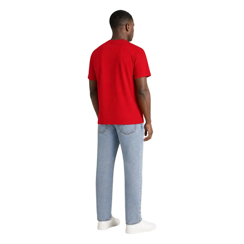 Ein Mann trägt ein rotes, kurzärmeliges T-Shirt aus Bio-Baumwolle von Tommy Hilfiger und hellblaue Jeans.